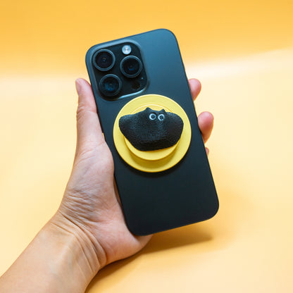 A MagSafe phone grip shaped like a climbing hold, featuring Black Meow the cat – a fun and functional gift for rock climbers and cat lovers.